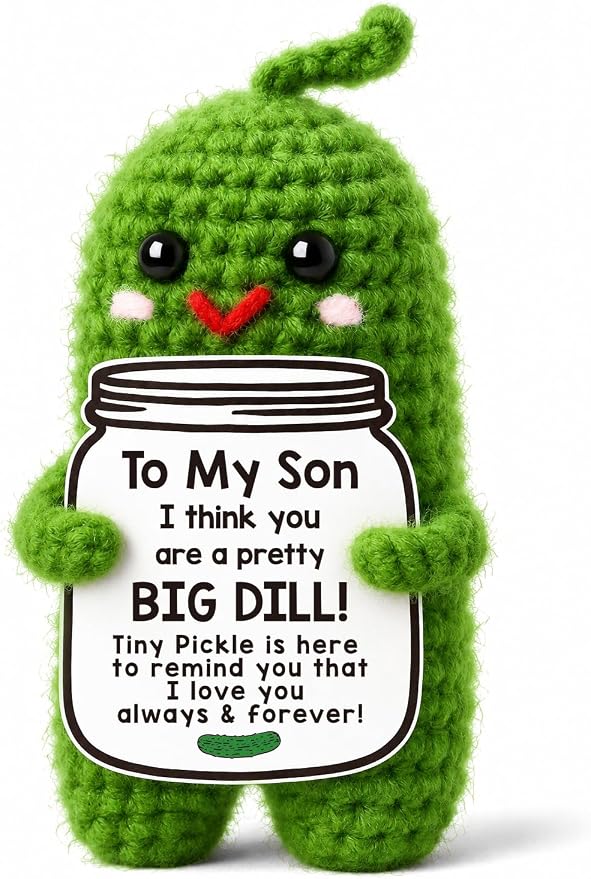 Small handmade green crochet pickle plush with rosy cheeks holding a sign with a sweet message for a son